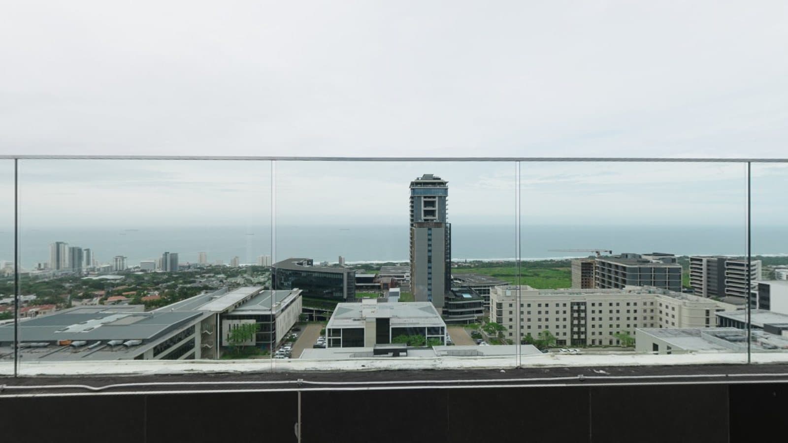 A rooftop view over a city behind a glass railing, a wide panoramic scene
